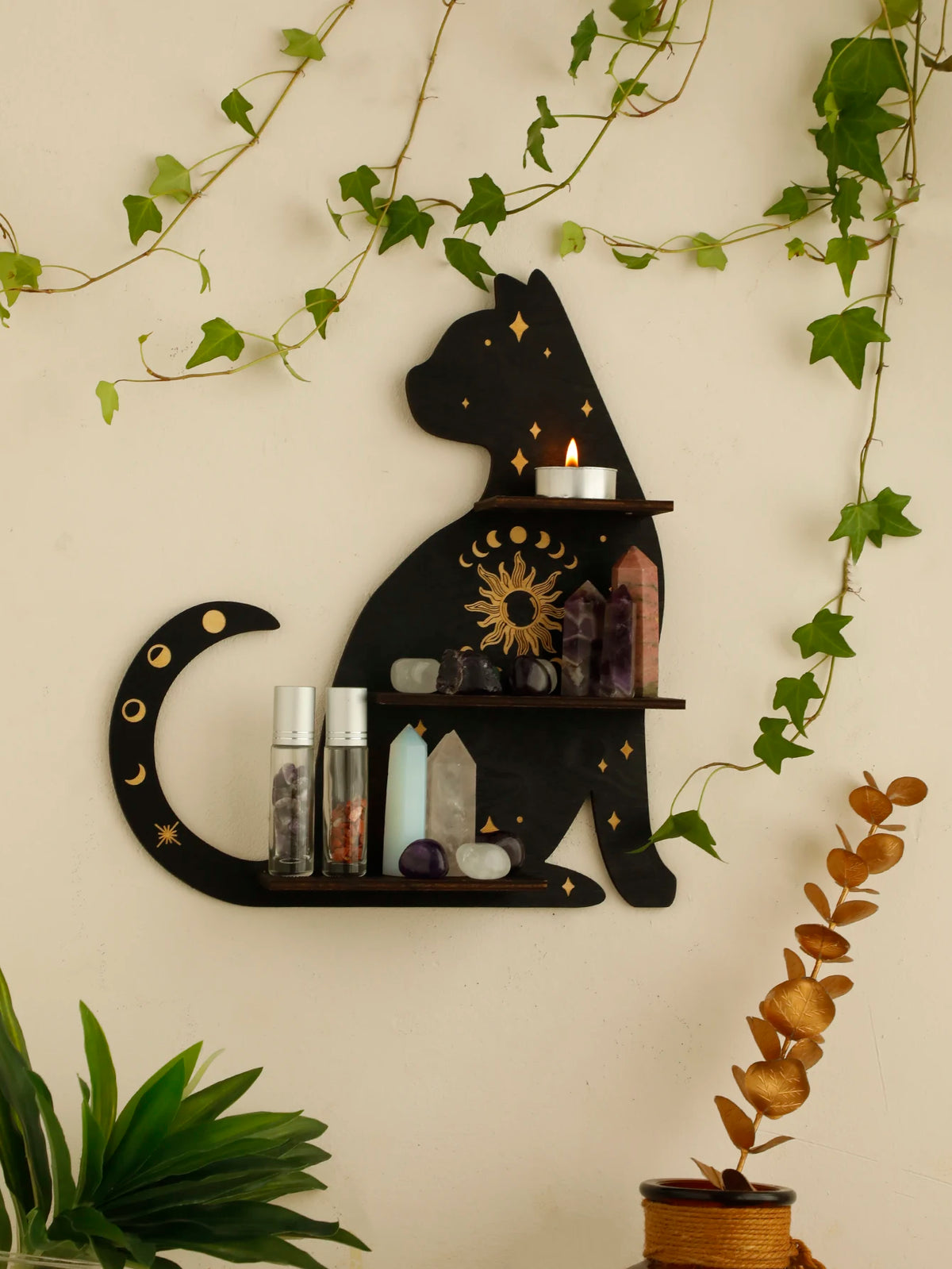 A black cat silhouette decoratively mounted on a floating shelf, featuring crystals and a lit candle, surrounded by green vin