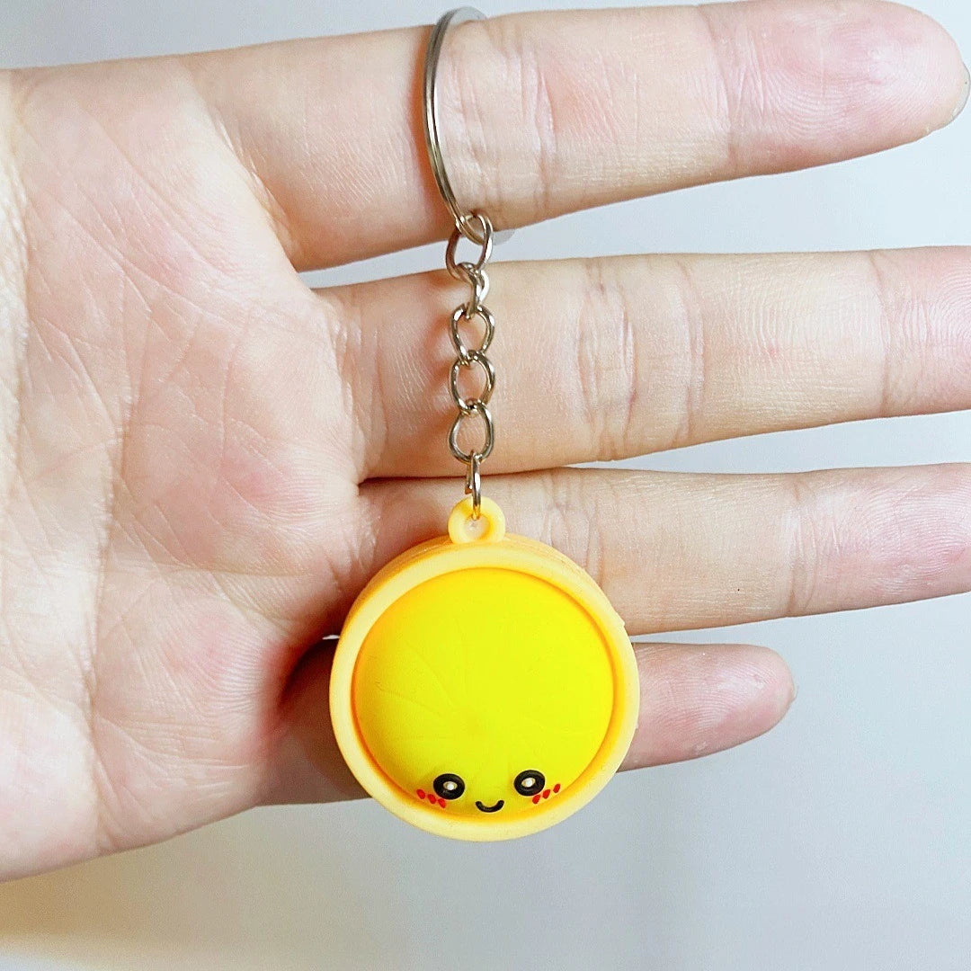 Eine Hand hält einen gelben, runden Anhänger mit lächelndem Gesicht an einer silbernen Kette.