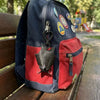 A navy blue backpack featuring a red pocket with a black bat charm and various round key rings.