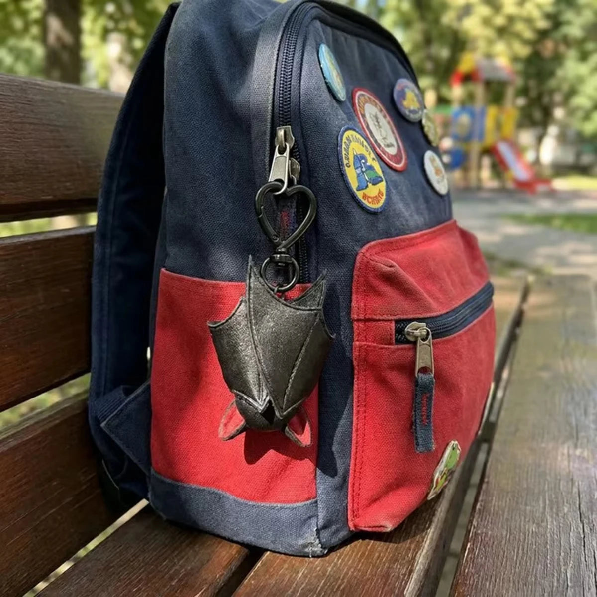 A navy blue backpack featuring a red pocket with a black bat charm and various enamel pins.