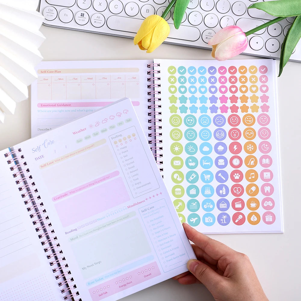 An open self-care journal with pages for planning, mood tracking, and daily happiness stickers.