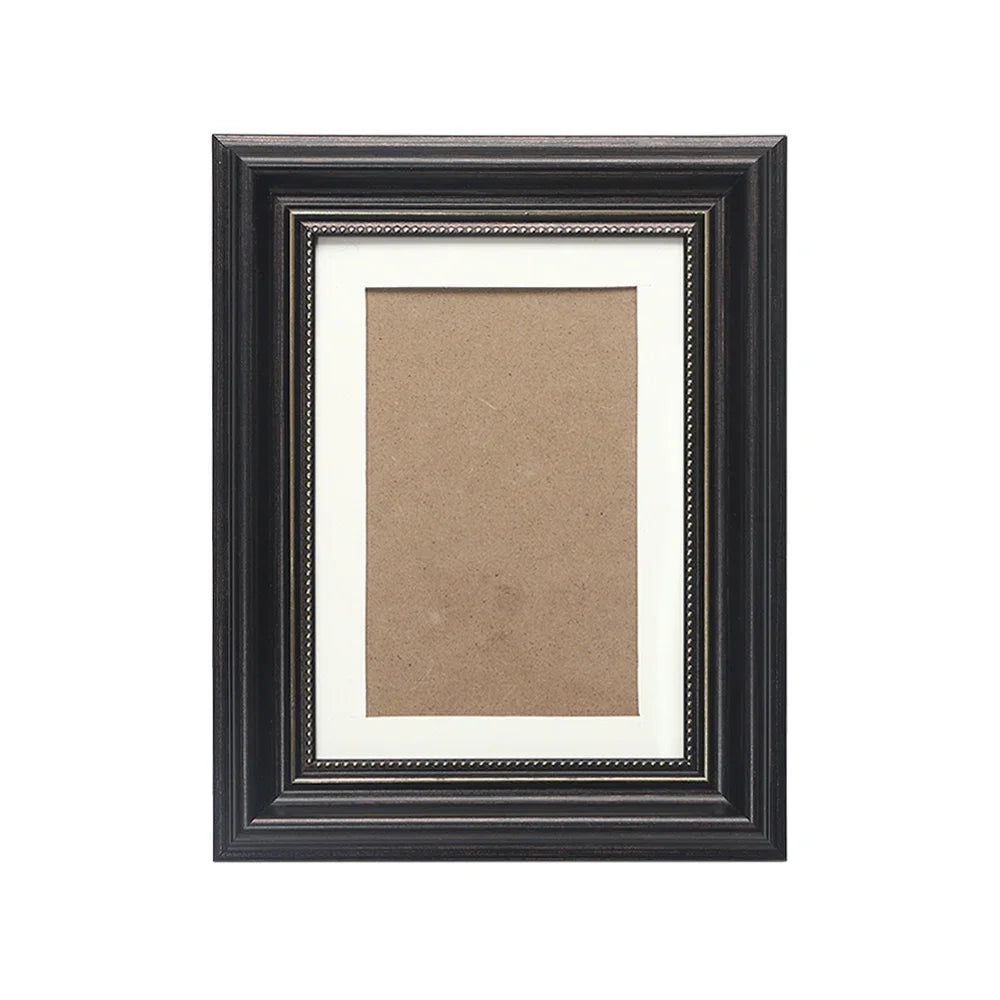 A dark wood photo frame with an antique gold trim, featuring a light brown mat and a photograph.