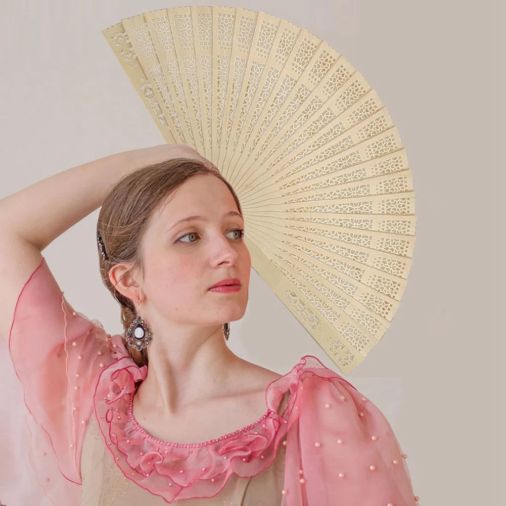 A woman holds a large, light yellow wooden folding hand fan against a pale background.