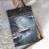 A framed print of a racing car driving on a track with blurred lights and spectators, set in a cardboard box.