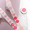Eine Rolle runder pinker und roter Dankeschön-Sticker neben einer klaren Flasche.