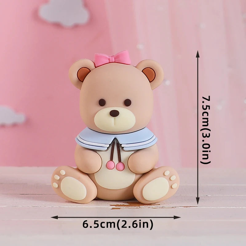 A cute beige bear baby block topper with pink accents sitting on a light wooden surface.