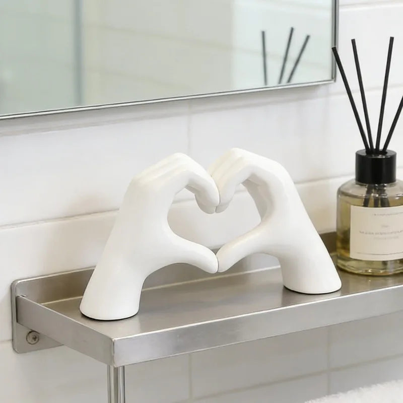 A white heart shape sculpture made of hands rests on a metal shelf in front of a tiled backsplash.