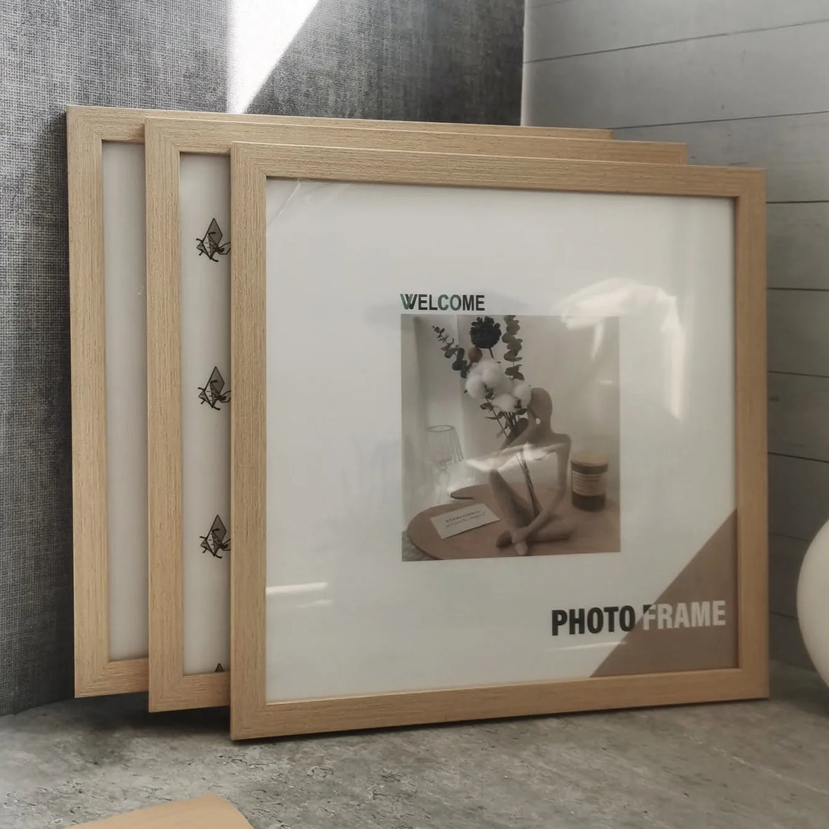 A set of three light wood photo frames with glass fronts and decorative elements displayed on a gray surface.