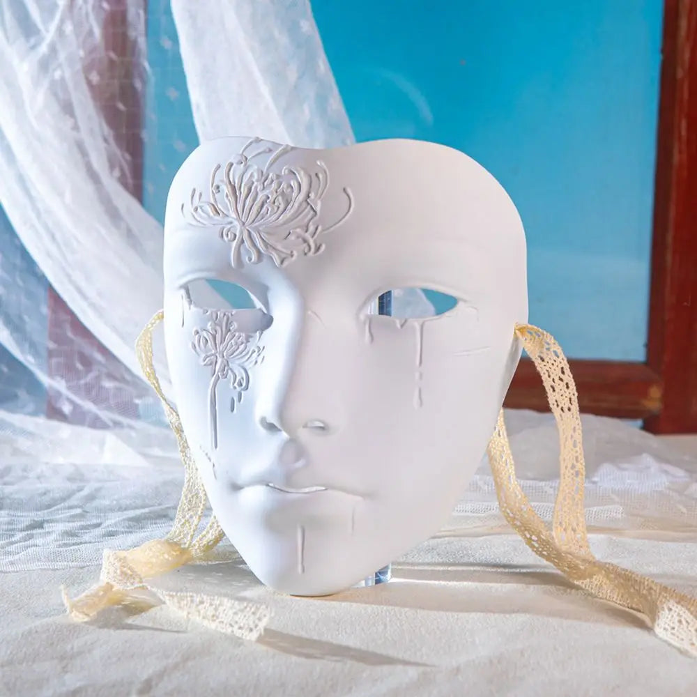 A white ancient style masquerade mask with intricate floral designs is displayed on a white cloth.