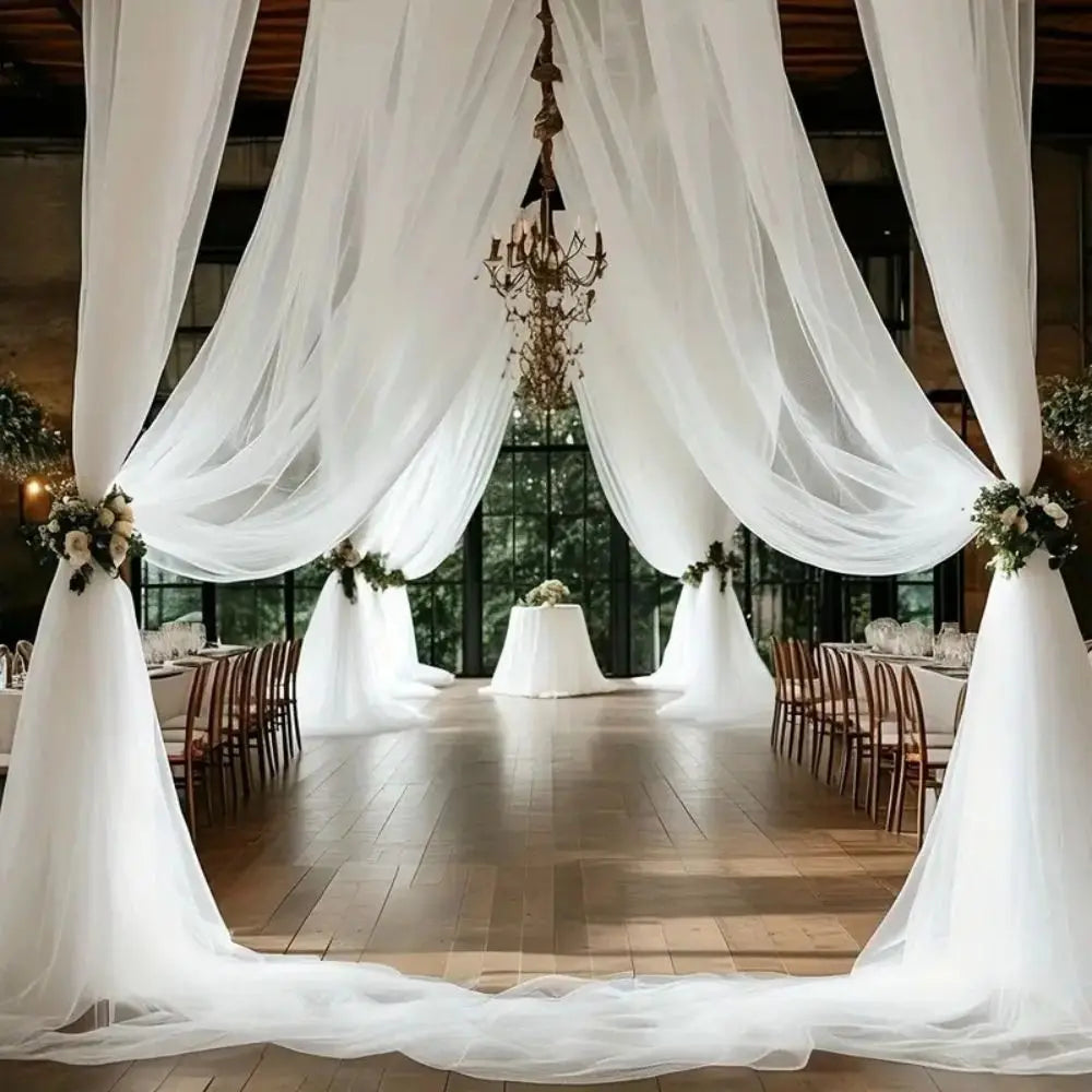 Elegant wedding setup featuring sheer white tulle fabric draping a venue with chandeliers and wooden chairs.