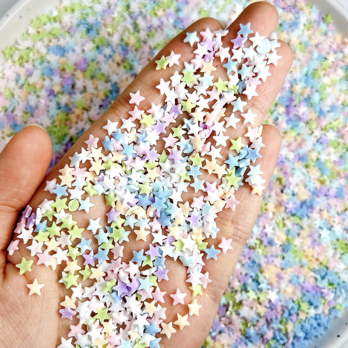 Una mano esparciendo adornos de uñas de tortugas mini coloridas sobre una superficie.