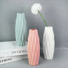 Three tall decorative plastic vases in mint green, pink, and white with a white flower stem.