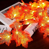Bright orange maple leaf string lights illuminating autumn leaves on a dark surface.