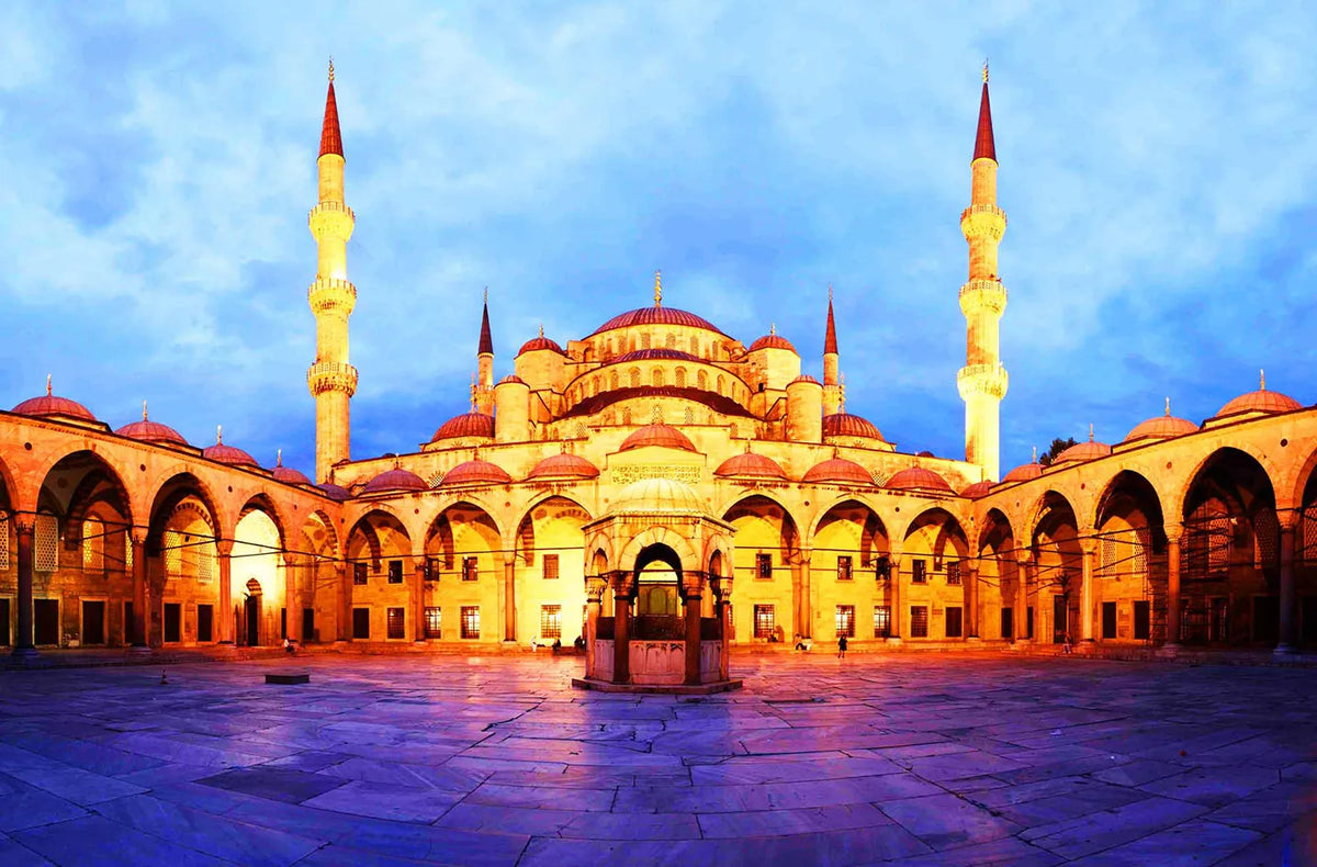 A large, golden-yellow Islamic mosque with domes and minarets under a blue sky.