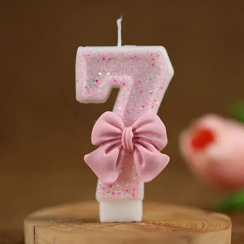 A pink glitter candle shaped like the number seven with a bow decoration