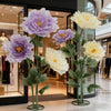 Large artificial silk purple and yellow poppy flowers displayed on a stand in a retail setting.