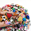 A hand holds a collection of colorful PVC shoe charms for clogs and slides featuring various animal and food designs.