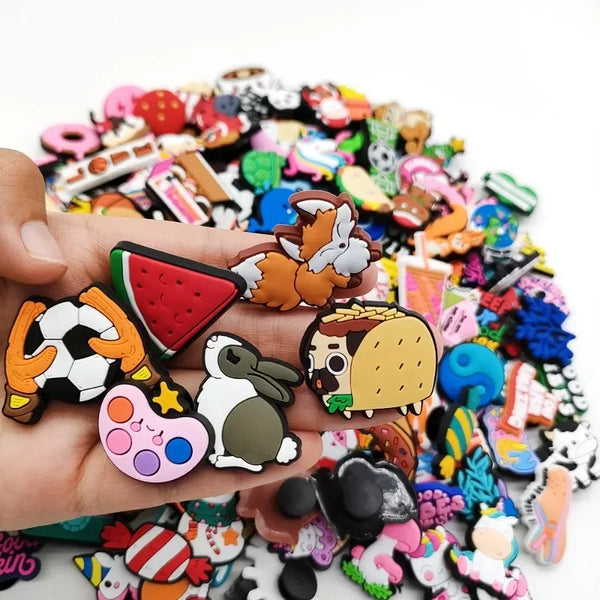 A hand holds a collection of colorful PVC shoe charms for clogs and slides featuring various animal and food designs.