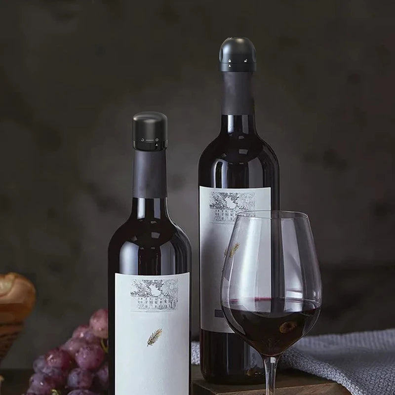 A dark red wine bottle is shown next to a glass of red wine and a bunch of grapes.