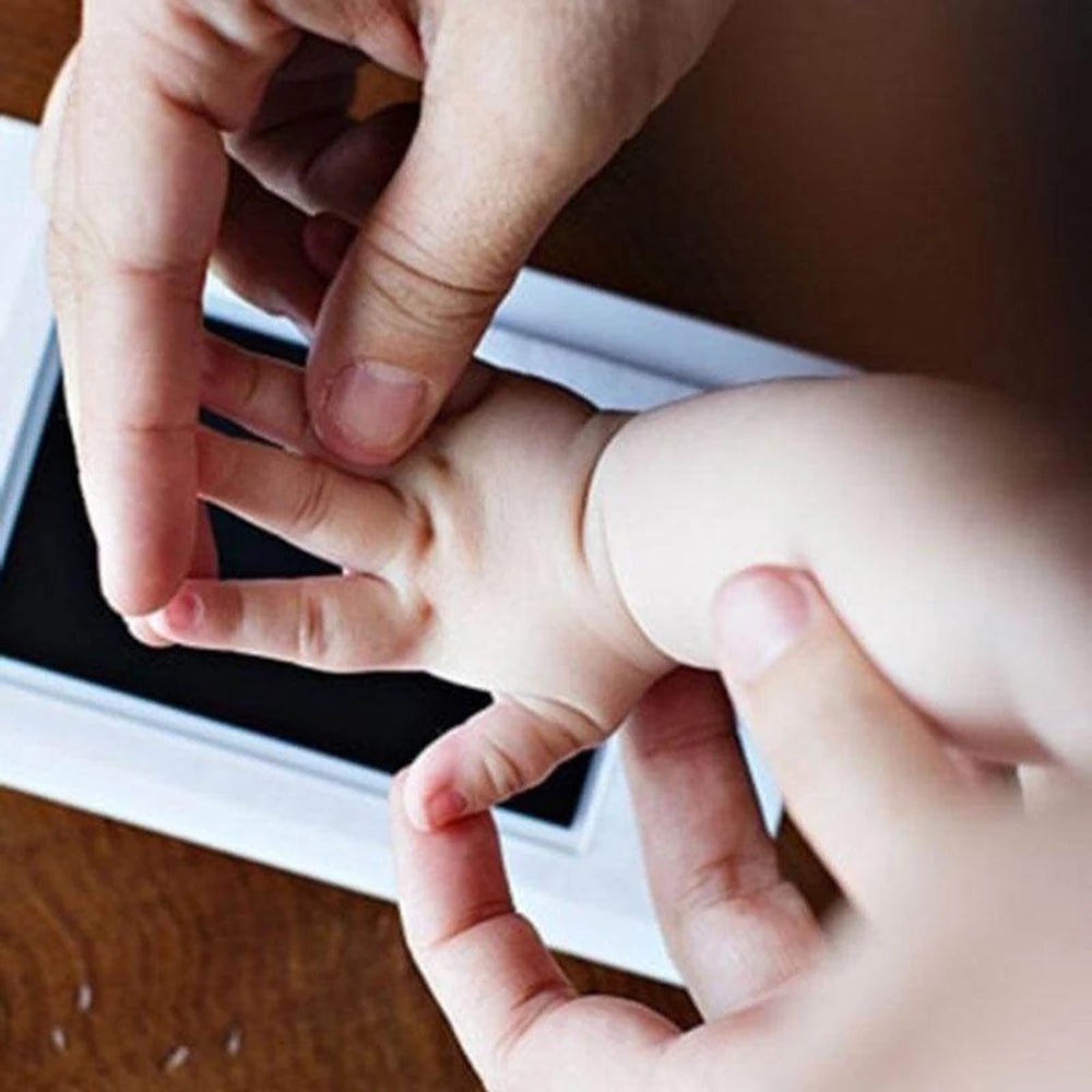 A hand is pressing a baby's hand onto a photo frame to create a handprint memory.