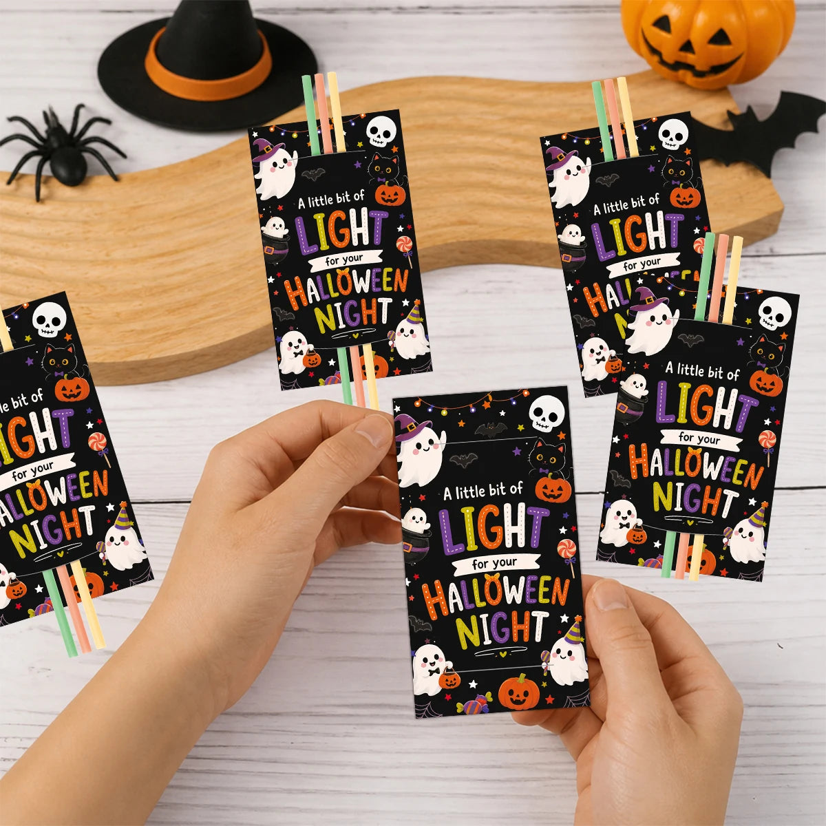 A hand holds a Halloween glow stick holder card featuring a ghost and pumpkin design.