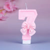 A pink glittery number seven candle decorated with a pink bow on a white base.