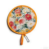 A round fabric fan with a floral pattern in pink, yellow, and green on a wooden handle.