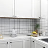 White kitchen cabinets and countertops with black subway tile backsplash and greenery.