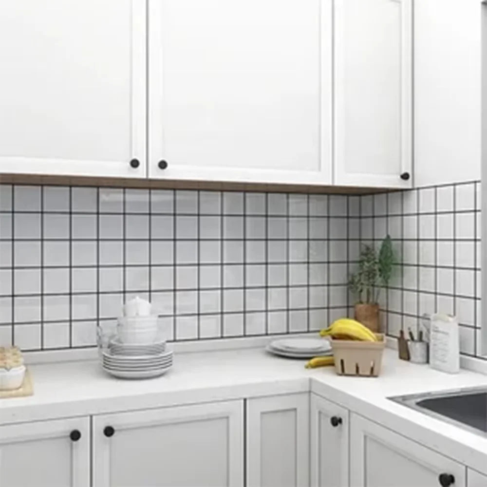 White kitchen cabinets and countertops with black subway tile backsplash and greenery.