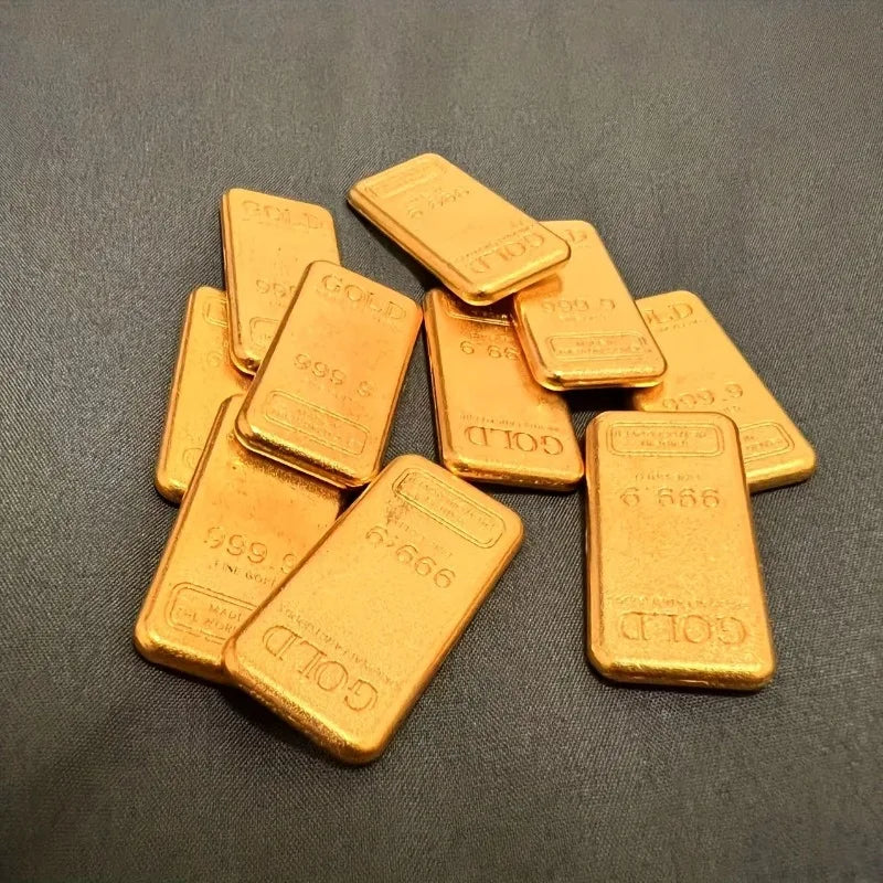 A collection of ten small, rectangular gold-colored simulated ingot fortune charms arranged on a dark surface.