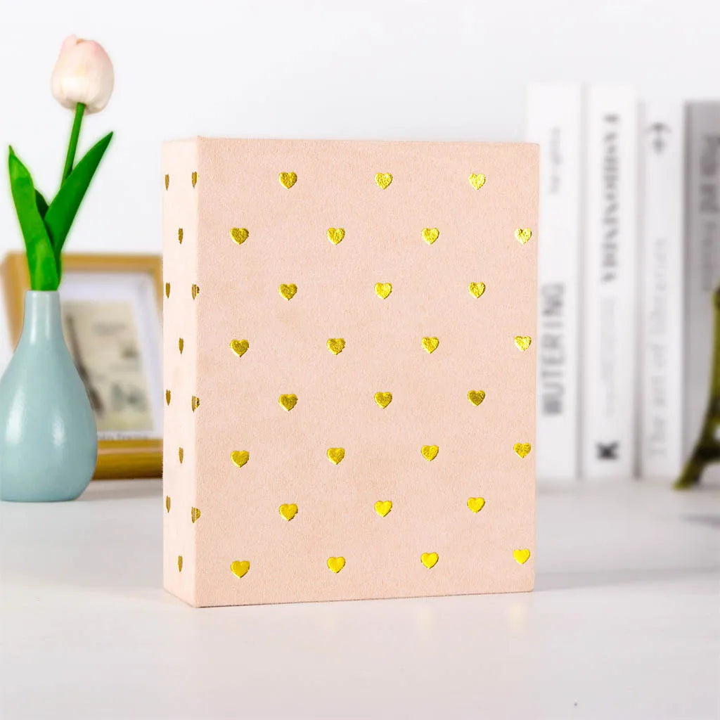 A pink photo album with gold foil hearts rests next to a single white tulip.