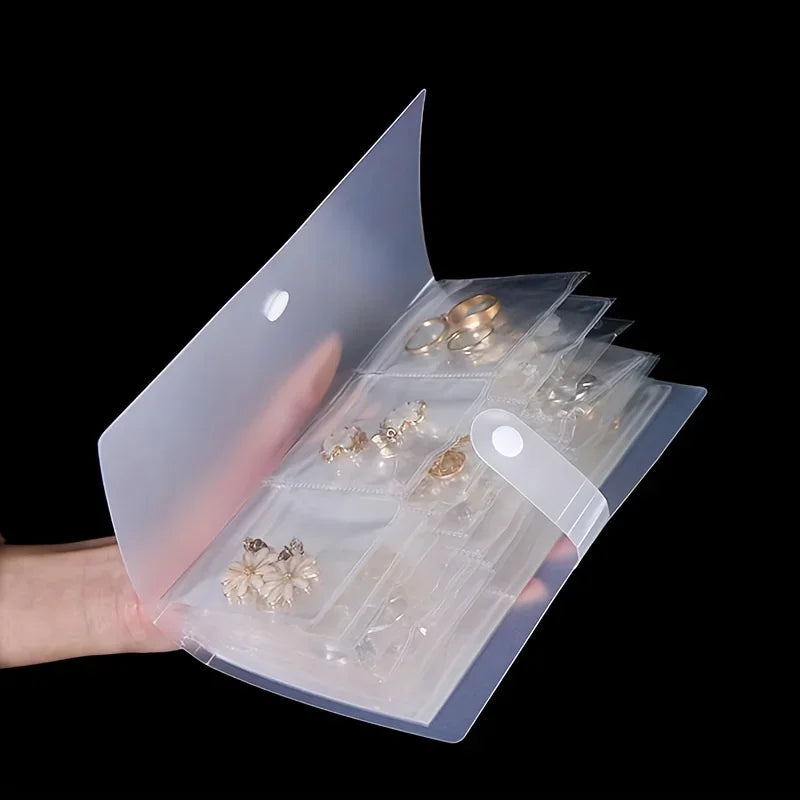 A transparent jewelry organizer storage bag with multiple grids holding small gold-toned jewelry pieces.