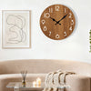 A minimalist wooden wall clock with a dark face hangs above a light beige sofa and glass table.