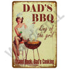 A vintage metal sign featuring a woman cooking BBQ, with text that reads Dad's BBQ king of the grill and Stand back Dad's Coo