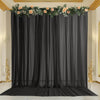 A floor-to-ceiling black chiffon backdrop curtain decorated with floral greenery and peach roses for an event.