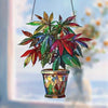 An acrylic floral pendant with green and red leaves hangs from a chain against a blurred background.