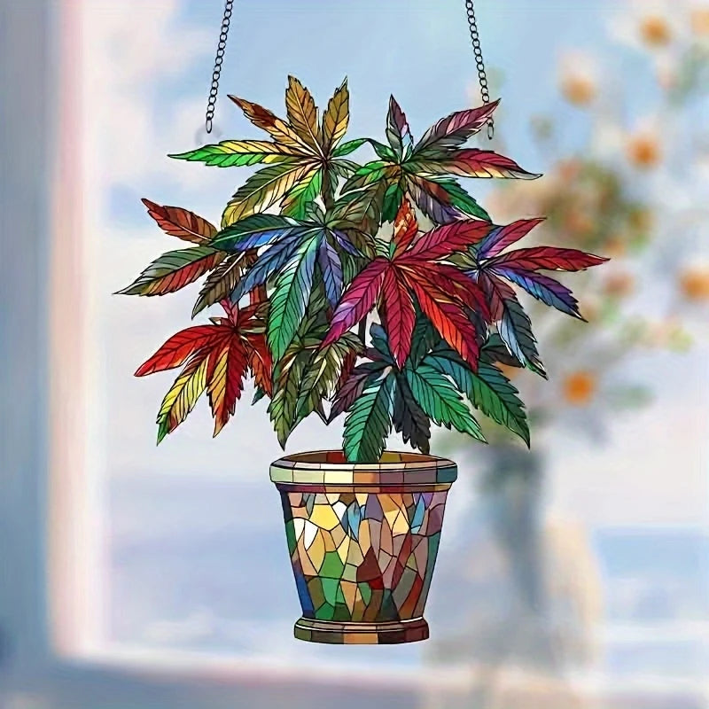 An acrylic floral pendant with green and red leaves hangs from a chain against a blurred background.