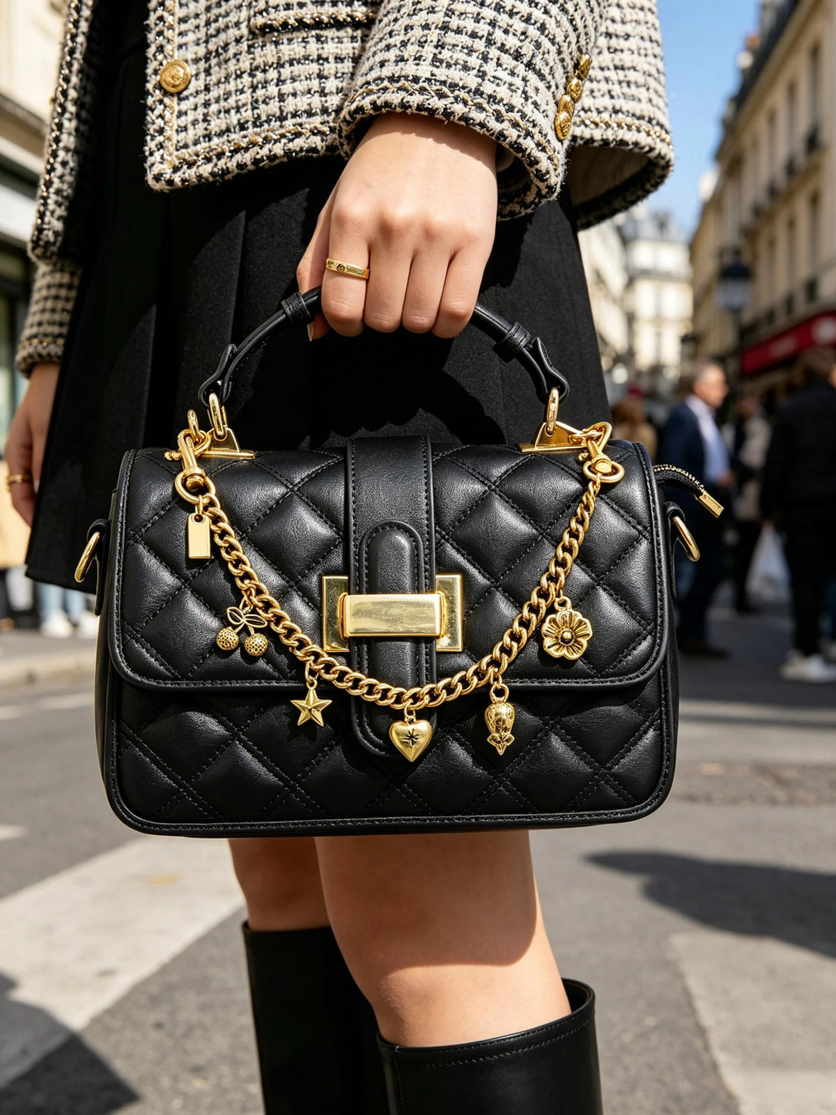 A woman holds a black quilted leather handbag with gold chain charms and a gold clasp.
