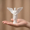 A white figurine of a praying angel with outstretched wings is held in an open hand.