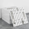 A stack of white marble peel-and-stick tiles with silver and gold accents displayed on a gray surface.