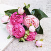 A bouquet of pink and magenta silk rose and peony artificial flowers with green leaves