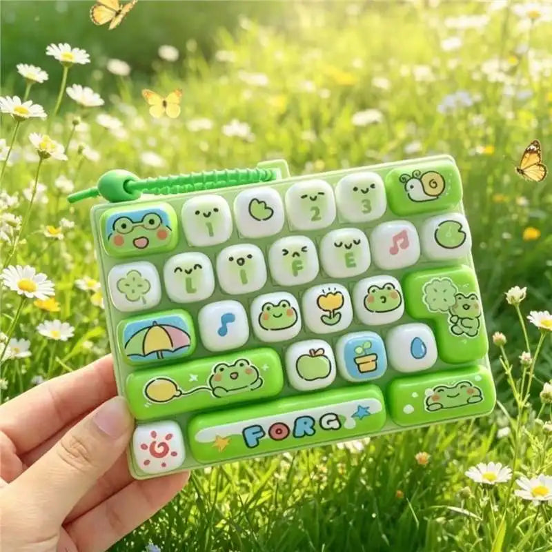 A hand holds a green silicone keyboard keycap keychain featuring various cartoon animal and food icons.