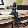 A black desktop figurine of a woman in a flowing gown with a veil, displayed on a wooden surface.