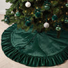 A deep emerald green velvet Christmas tree skirt with a ruffled edge and hanging ornaments.
