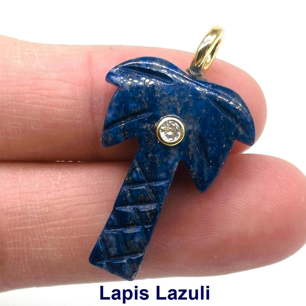 A deep blue lapis lazuli crystal pendant with a gold bail and a clear zircon charm, held by a finger.
