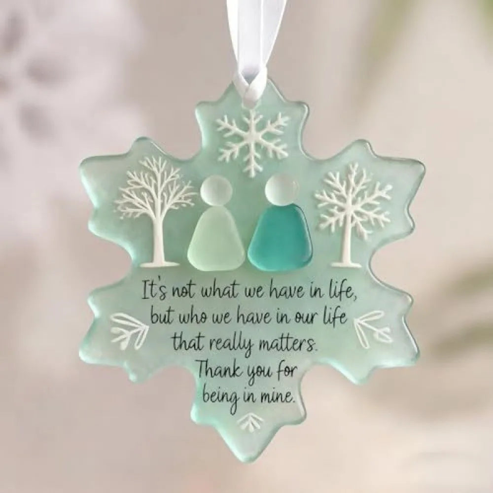 A light mint green acrylic snowflake pendant featuring white tree designs and a message about valuing relationships.
