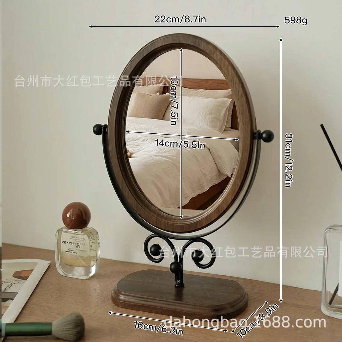 An oval vanity mirror with a wooden frame and stand, showing a reflection of a bed.