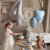 A young girl in a white dress interacts with large silver and blue heart-shaped foil balloons in a bright room.