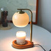 A brass aromatherapy wax melting lamp with a spherical glass shade and a candle sits on a white table.
