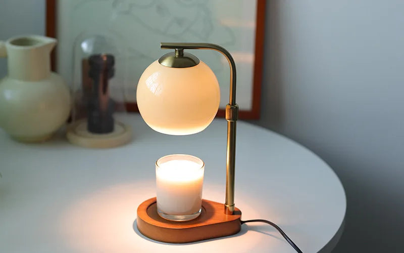A brass aromatherapy wax melting lamp with a spherical glass shade and a candle sits on a white table.
